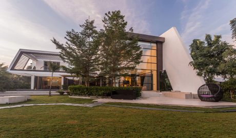 A modern, sleek building with geometric shapes, glass, and wood paneling, surrounded by lush greenery.