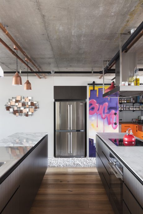 Sleek modern kitchen with concrete ceiling, track lighting, and vibrant wall art.