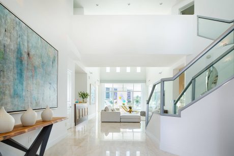 Spacious modern living area with white marble floors, large abstract artwork, and glass walls.