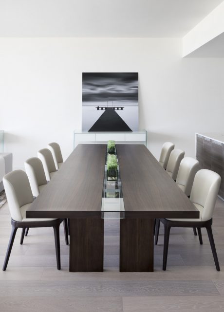 Minimalist dining room with large dark wood table, glass inserts, and abstract wall art.