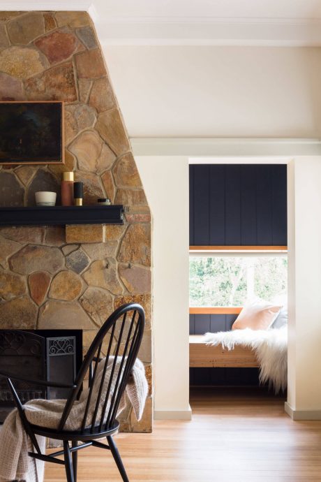 Rustic stone fireplace with black shelving and cozy window nook with dark curtains.