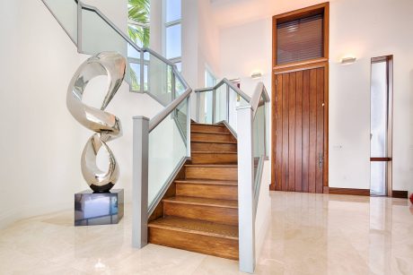 Modern staircase with glass railings, wooden steps, and abstract sculpture in foyer.