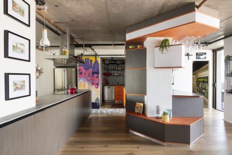 Open-concept kitchen and living area with concrete walls, industrial lighting, and colorful accents.