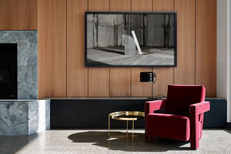 A modern living room with a large TV display, wooden wall panels, and a stylish red armchair.