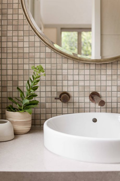 Serene bathroom with round mirror, tiled backsplash, and potted plant.