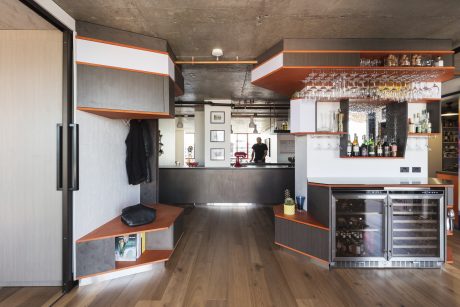 Sleek, modern kitchen with concrete walls, orange accents, and stainless steel appliances.
