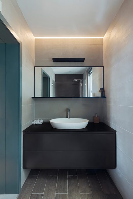 Contemporary bathroom with dark vanity, vessel sink, mirror, and recessed lighting.