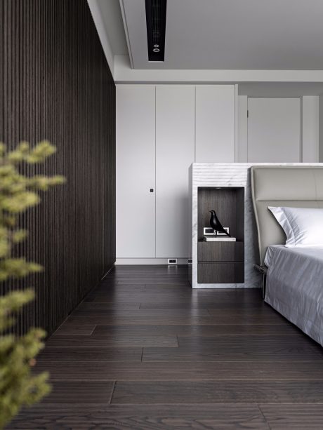 A modern and minimalist bedroom with a dark accent wall, recessed lighting, and a sleek wooden headboard.