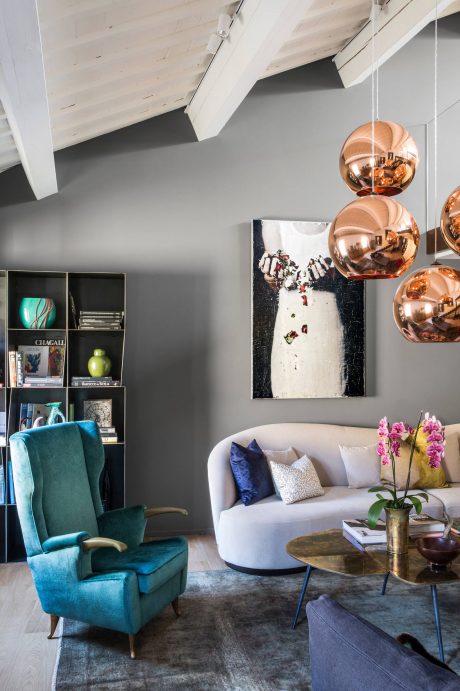 Cozy living space with plush turquoise armchair, modern light fixtures, and artistic decor.