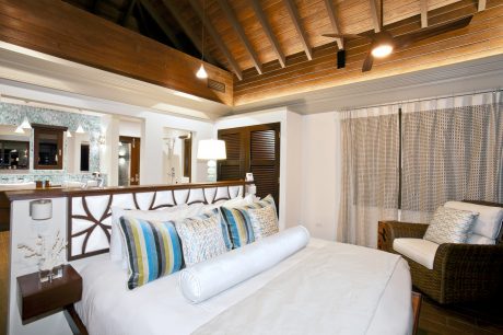 Cozy rustic bedroom with wooden beams, white linens, and tropical decor accents.