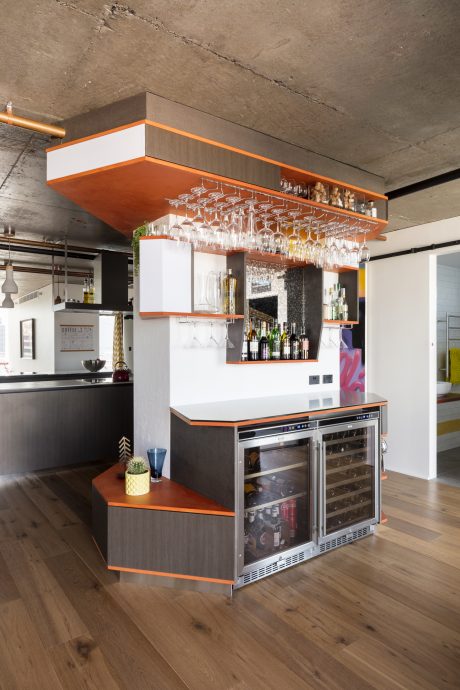 A modern, open-plan kitchen with a suspended glass storage rack and built-in wine cooler.