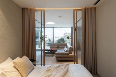 Contemporary living room with floor-to-ceiling glass doors, beige curtains, and modern furniture.