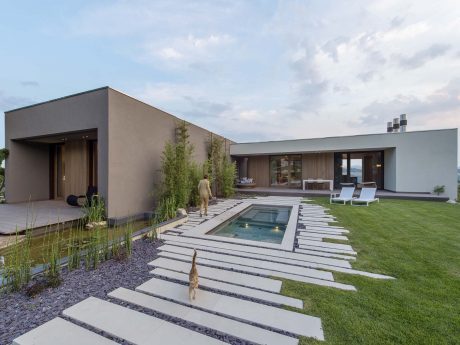Minimalist modern home with pool, patio, and stepping stone path through lush landscaping.