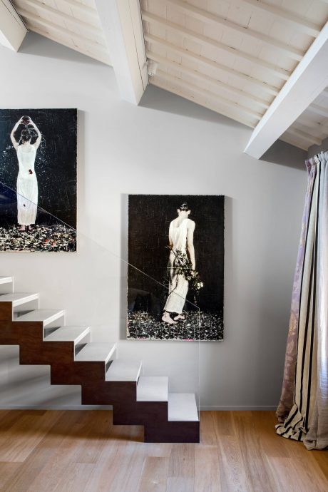 Modern staircase with wooden treads and white risers in a bright, minimalist interior featuring striking black and white artwork.