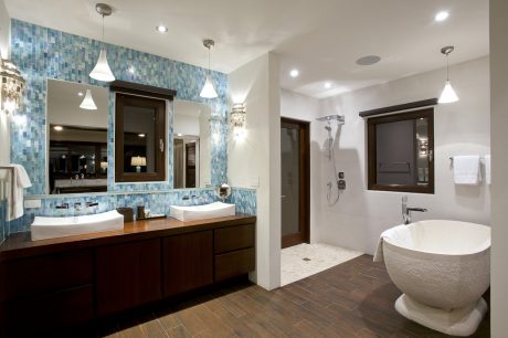 A modern bathroom with a blue mosaic tile wall, wood vanity, and freestanding tub.
