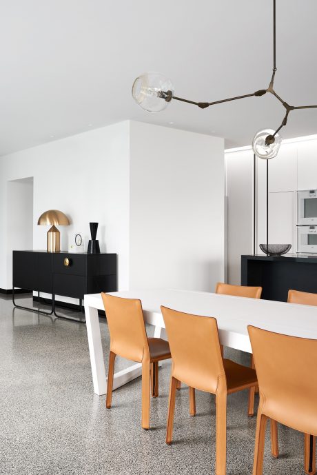 A modern dining room with white walls, a black credenza, and orange leather chairs around a white table.