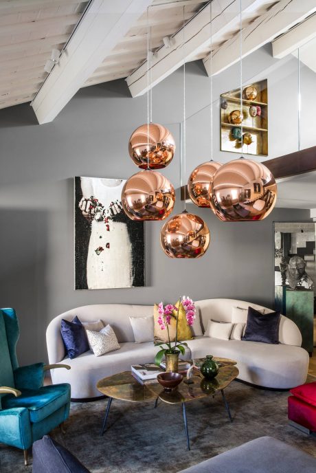 The room features a modern, eclectic design with copper pendant lights, a plush sofa, and abstract artwork.