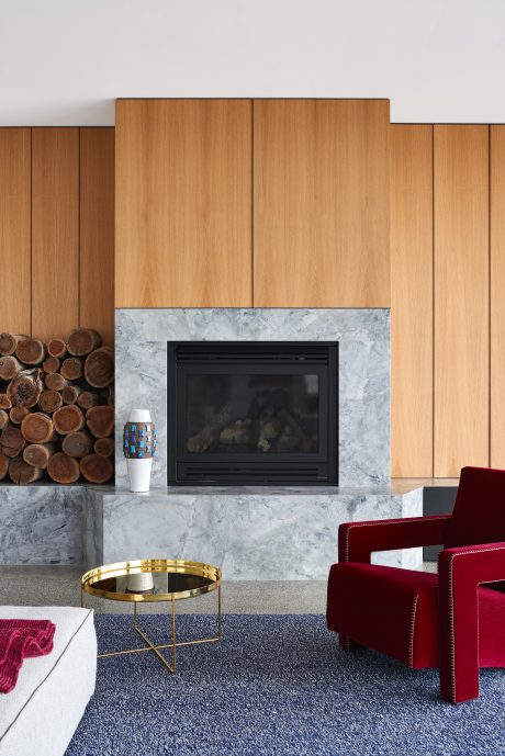Minimalist fireplace design with wooden panels, marble surround, and contemporary furnishings.