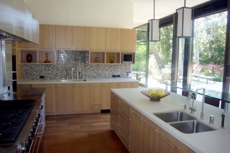 Contemporary kitchen with light wood cabinetry, mosaic backsplash, and glass doors overlooking nature.