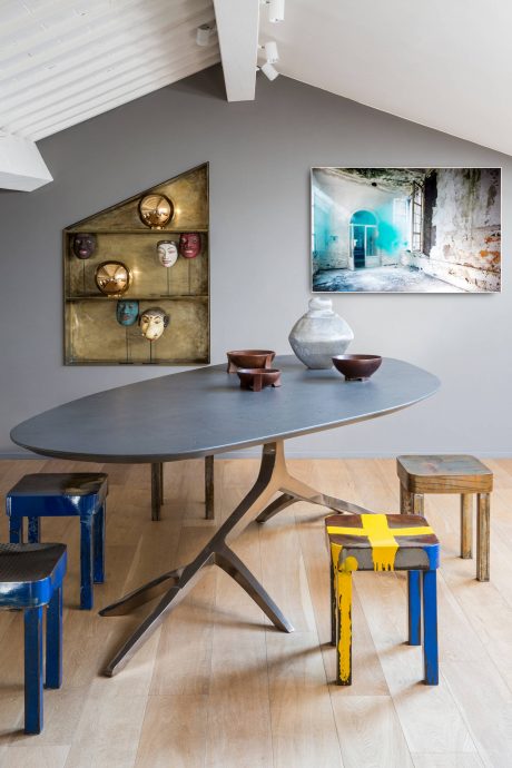 A modern dining area with a grey oval table, colorful stools, and eclectic wall decor.