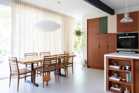 Modern open-plan kitchen and dining area with wooden furniture, pendant lamp, and built-in storage.