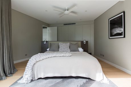 Cozy and modern bedroom with neutral tones, plush bedding, and a large ceiling fan.