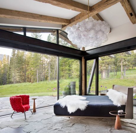 Rustic cabin interior with wood beams, floor-to-ceiling windows, and a modern light fixture.