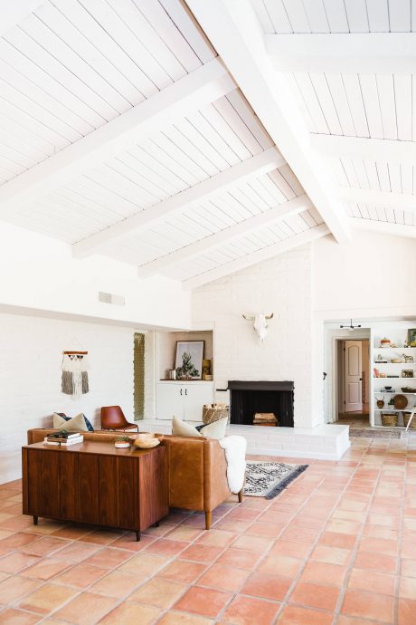 An airy, modern living room with a whitewashed wood ceiling, terracotta tile floor, and rustic furnishings.