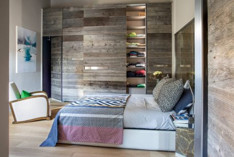 Rustic accent wall, wood-paneled closet, and stylish bedding in a modern bedroom.