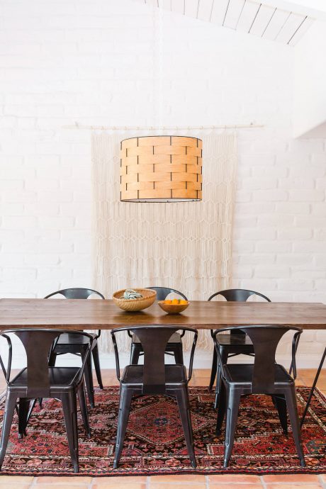 A dining room with a wooden table, black metal chairs, and a woven light fixture.