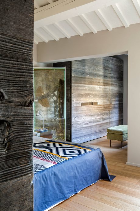 A modern bedroom with textured walls, wooden paneling, and a patterned bedspread.