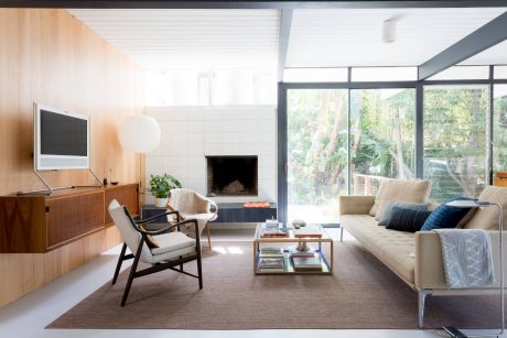 Mid-century modern living room with floor-to-ceiling windows, cozy furniture, and natural elements.