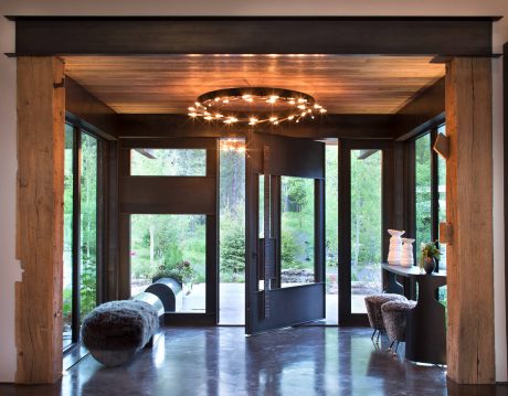 Spacious, modern entryway with wooden beams, circular lighting fixture, and floor-to-ceiling windows.
