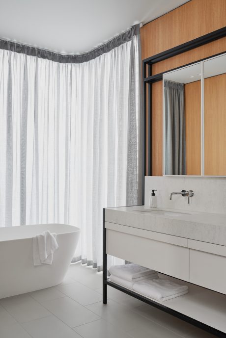 A modern bathroom with a wooden accent wall, curved curtains, and a minimalist vanity.