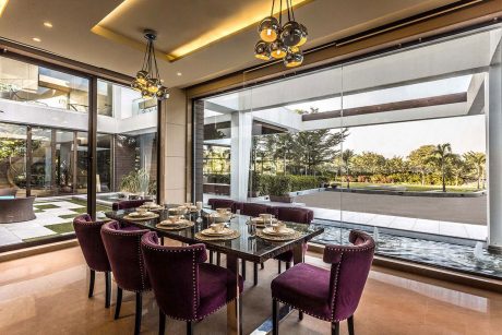 A modern, luxurious dining room with glass walls, plush purple chairs, and a chandelier.