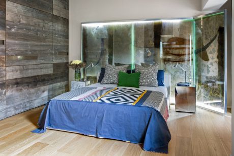 Rustic wood walls, modern glass accents, graphic bedding, and warm wood floors in this bedroom.