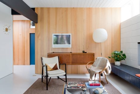 A cozy mid-century modern living room with warm wood paneling, retro furniture, and a sleek TV.