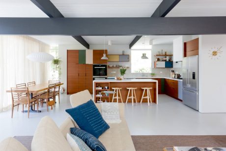 Modern open-plan kitchen, dining, and living space with colorful cabinetry and wood accents.