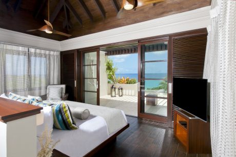Spacious bedroom with wooden beams, sliding glass doors overlooking the ocean.