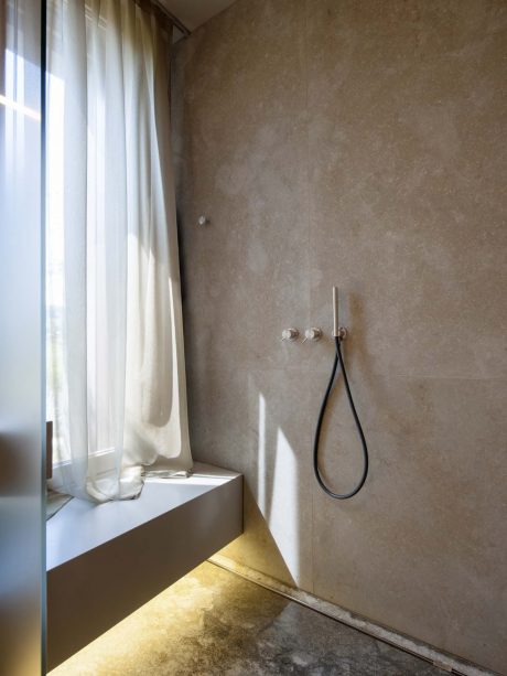 A minimalist bathroom with a concrete wall, a large window, and a simple showerhead.
