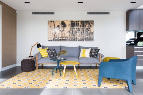 Bright living room with contemporary gray sofa, yellow accents, and patterned area rug.