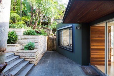 A lush, tropical garden setting surrounds a modern home featuring a wooden exterior and large windows.