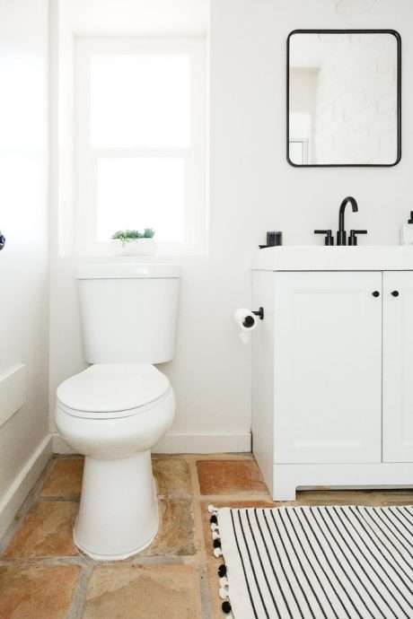 A minimalist bathroom with white walls, a rectangular mirror, and a patterned floor mat.