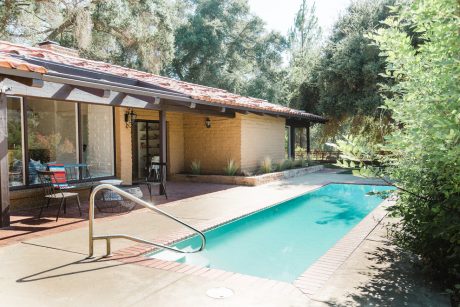 A cozy adobe-style home with a sparkling pool surrounded by lush greenery.