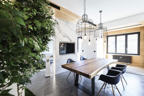 Modern dining room with wooden table, wire pendant lights, and indoor plant feature wall.