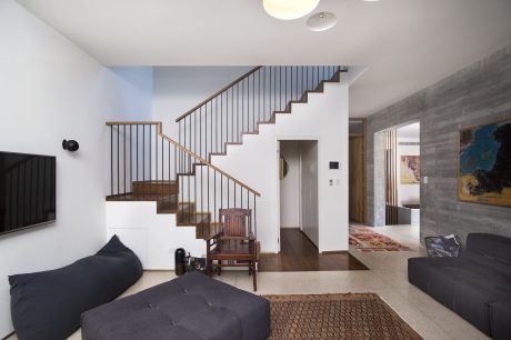 A modern, open-concept living space with wooden stairs, metal railings, and a mix of furniture.