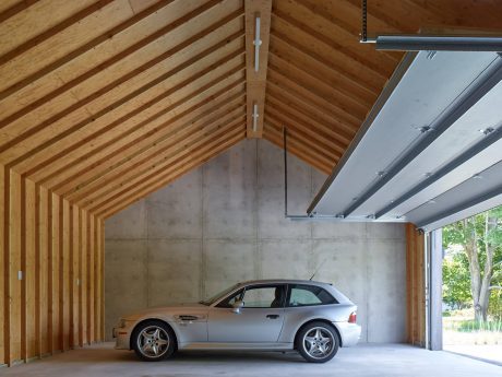 A modern wooden barn structure with a concrete wall and a silver car parked inside.