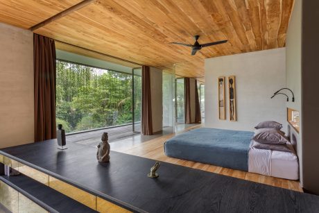 Rustic wood-paneled bedroom with large windows overlooking lush greenery.