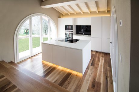 Spacious kitchen with large arched window, modern white cabinets, and wood flooring.