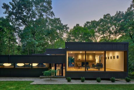 Modern cabin-style home with clean lines, large windows, and a wooden deck surrounded by lush greenery.